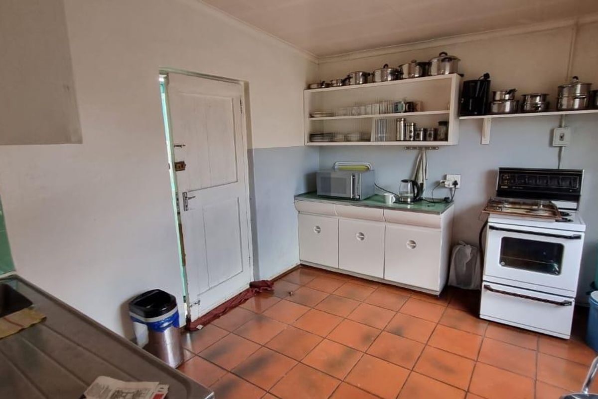 A functional kitchen featuring tiled flooring, built-in cabinetry, a freestanding stove, and a stainless steel sink with exposed plumbing.