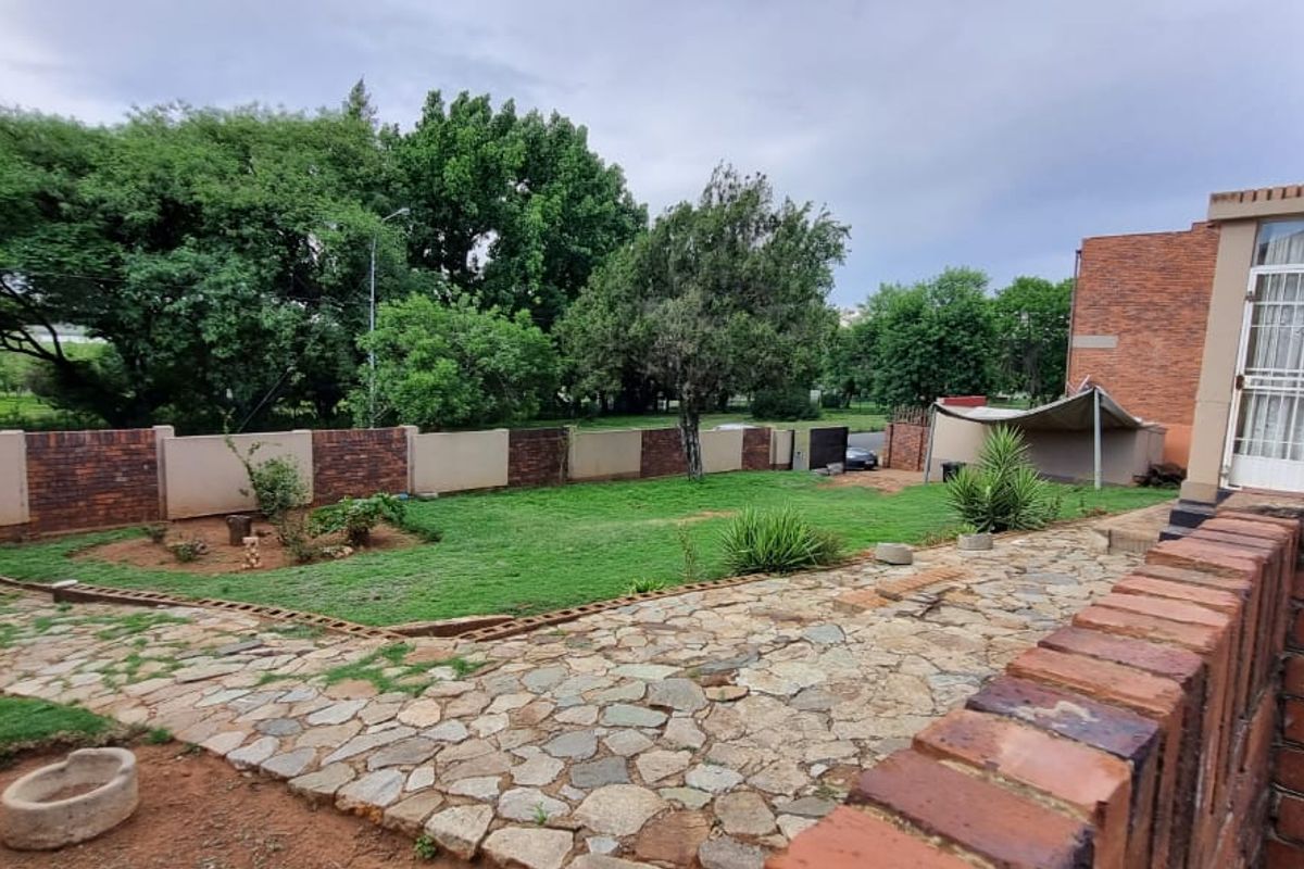 A spacious rear garden featuring a stone-paved patio area, established lawn, and perimeter brick walling, offering a private outdoor space.