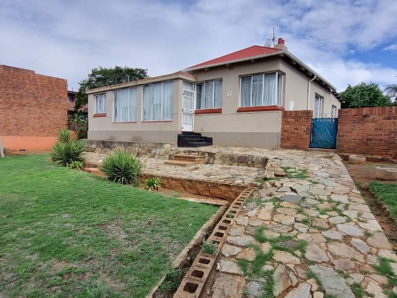 A detached house featuring a red metal roof, stone-paved patio area, and a spacious garden with a brick boundary wall.
