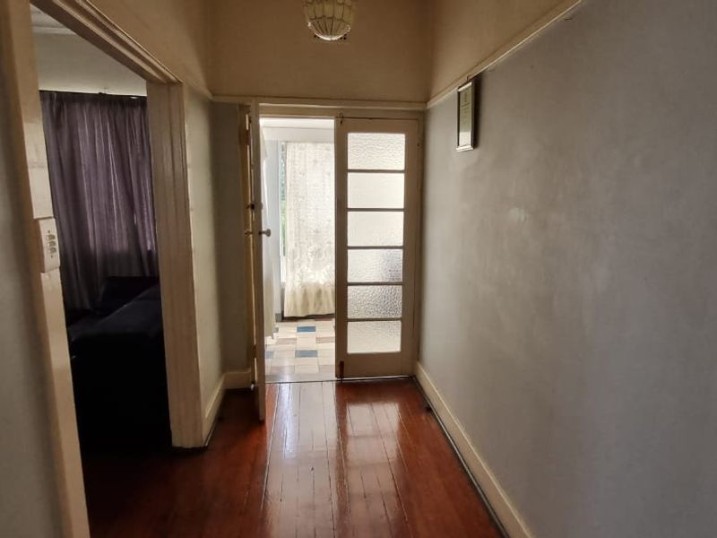 A traditional interior hallway featuring polished timber flooring, picture rails, and a glass-paneled door leading to an adjacent room.