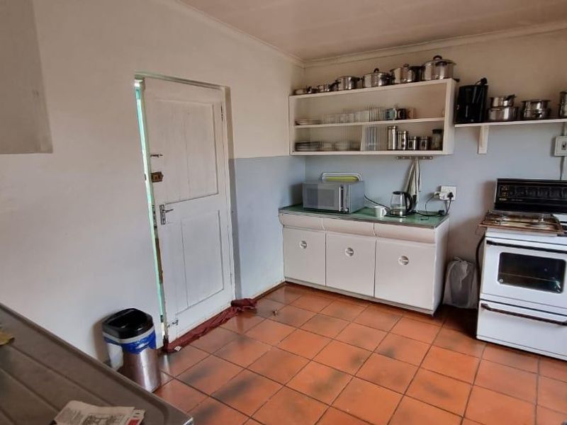 A functional kitchen featuring tiled flooring, built-in cabinetry, a freestanding stove, and a stainless steel sink with exposed plumbing.