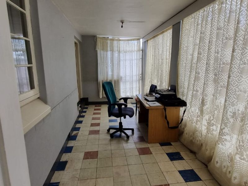 A sunroom or enclosed patio area featuring tiled flooring and large windows, currently utilized as a home office space.