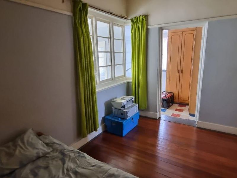 A bedroom featuring original timber flooring, large bay windows, and an adjacent walk-in closet area with built-in cabinetry.