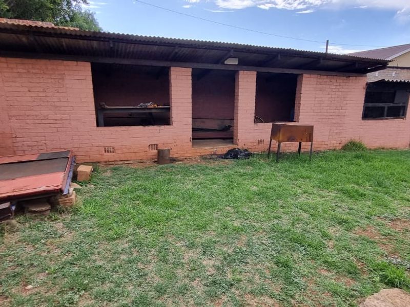 Rear exterior view of a brick outbuilding featuring open-plan utility spaces and a grassed backyard area.