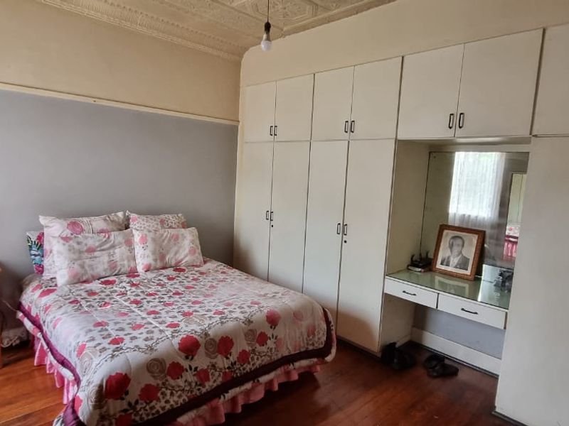 A bedroom featuring original timber flooring, a decorative pressed metal ceiling, and extensive built-in cabinetry with an integrated vanity mirror.