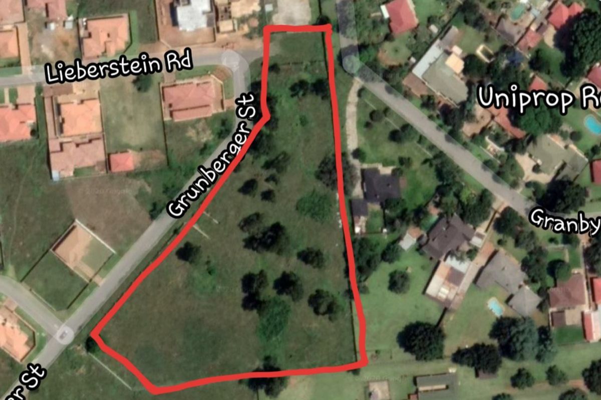 Aerial view of a vacant residential plot located on a corner stand, featuring established trees and surrounding neighborhood infrastructure.