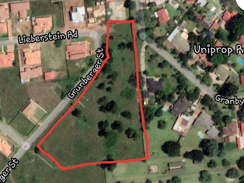Aerial view of a vacant residential plot located on a corner stand, featuring established trees and surrounding neighborhood infrastructure.