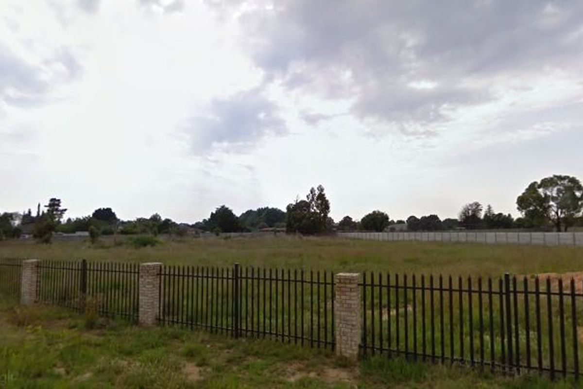 A vacant residential plot featuring perimeter brick and metal fencing and a concrete boundary wall.