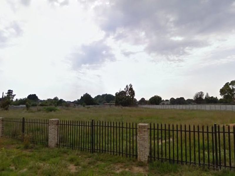 A vacant residential plot featuring perimeter brick and metal fencing and a concrete boundary wall.