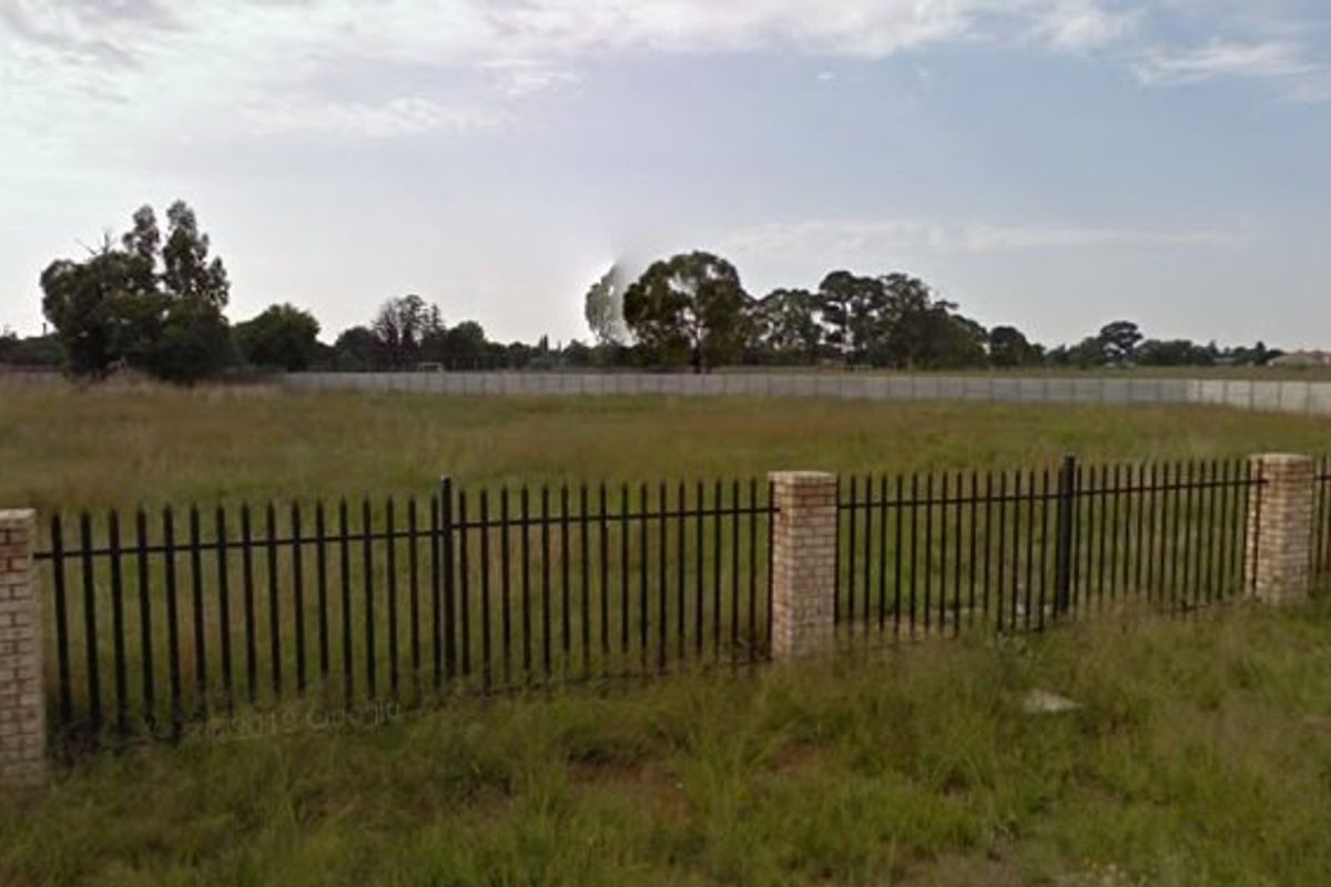 A vacant residential plot featuring established perimeter fencing with brick pillars and metal palisade panels, offering a clear view of the open land.
