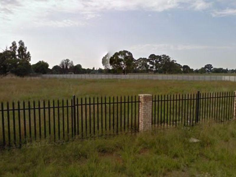 A vacant residential plot featuring established perimeter fencing with brick pillars and metal palisade panels, offering a clear view of the open land.