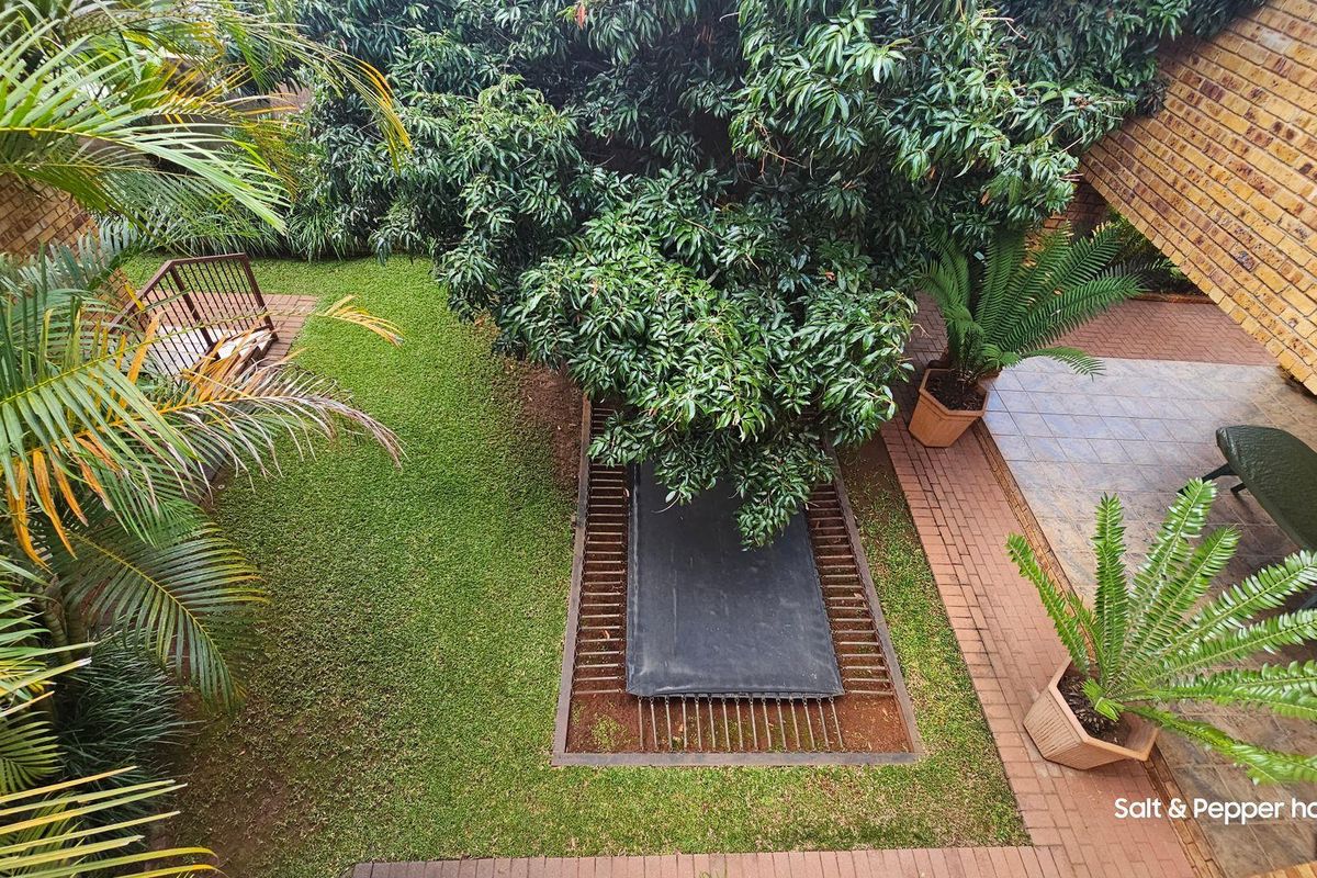 An elevated view of a private rear garden featuring a paved patio area, established trees, and a lawn.