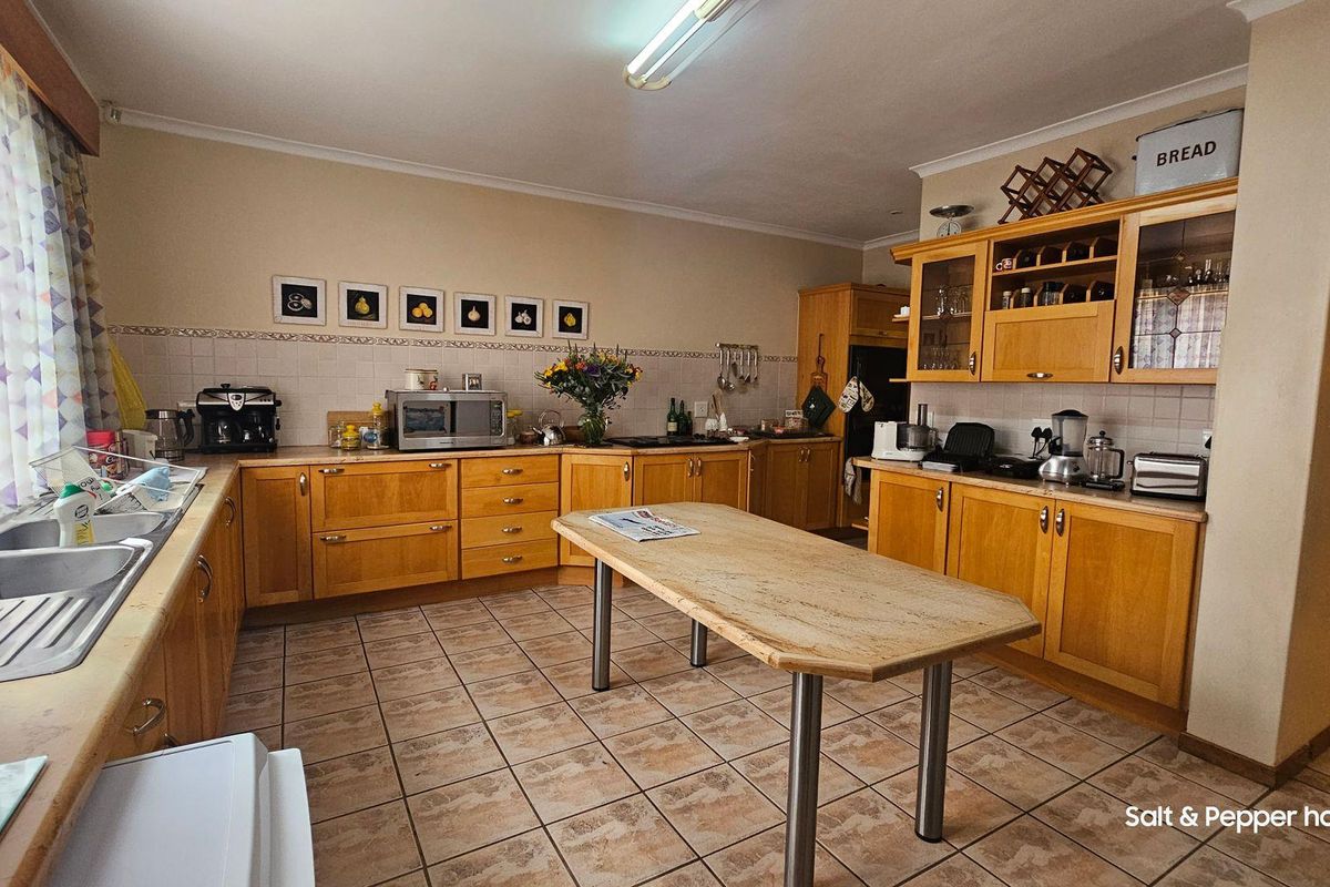 A functional kitchen featuring wooden cabinetry, tiled flooring, a central island, and a double stainless steel sink with a tiled backsplash.