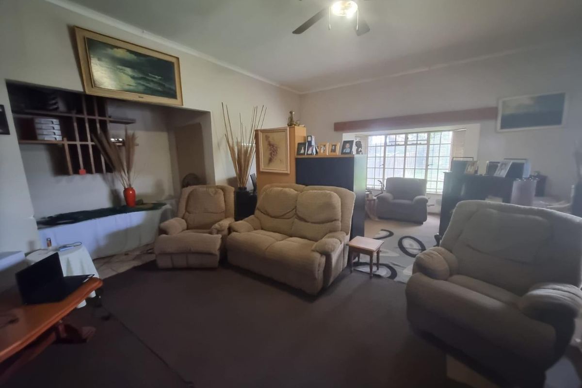 Spacious living room featuring a ceiling fan, built-in shelving unit, and large windows allowing for natural light.