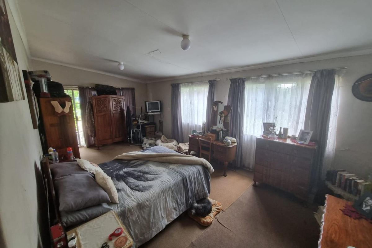 A spacious bedroom featuring large windows, neutral wall tones, and carpeted flooring, offering a functional layout with direct access to an outdoor area.