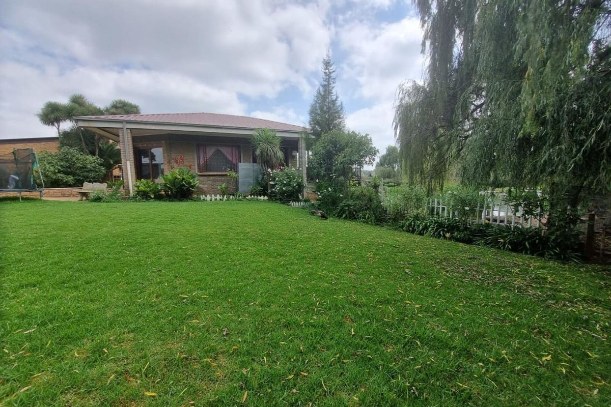 A view of the rear garden featuring a well-maintained lawn, mature trees, and a covered patio area attached to the brick farmhouse structure.