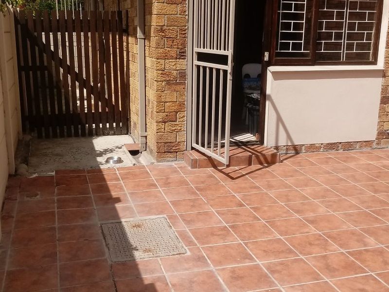 A paved outdoor patio area featuring a security gate, timber side gate, and brick exterior wall finishes.