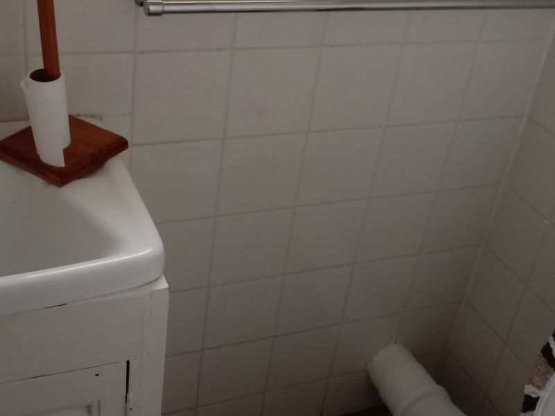 A compact bathroom featuring a vanity basin, toilet, and tiled walls, showing signs of age and wear in the finishes.