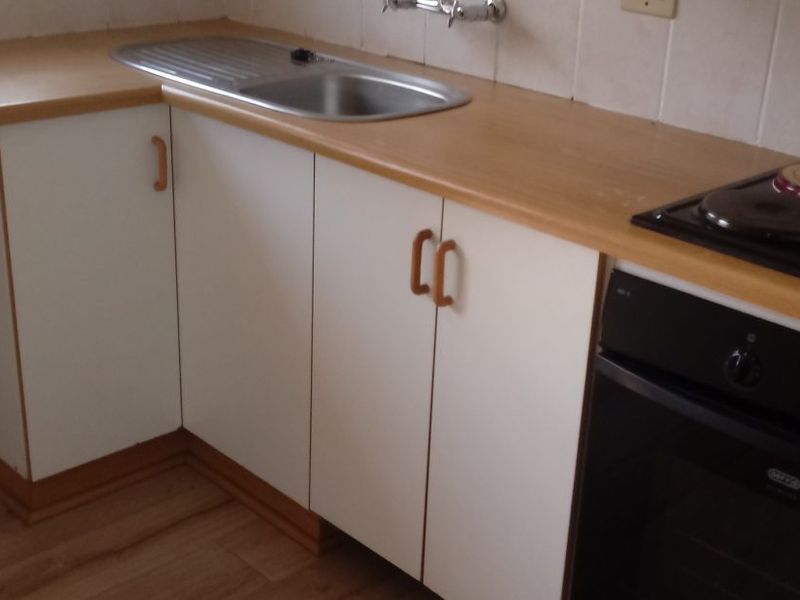 A functional kitchen area featuring laminate countertops, a stainless steel sink, built-in oven, electric hob, and tiled splashback.