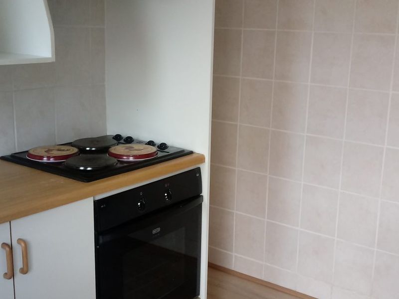 A functional kitchen area featuring a built-in oven, electric hob, tiled splashback, and laminate countertop with base cabinetry.