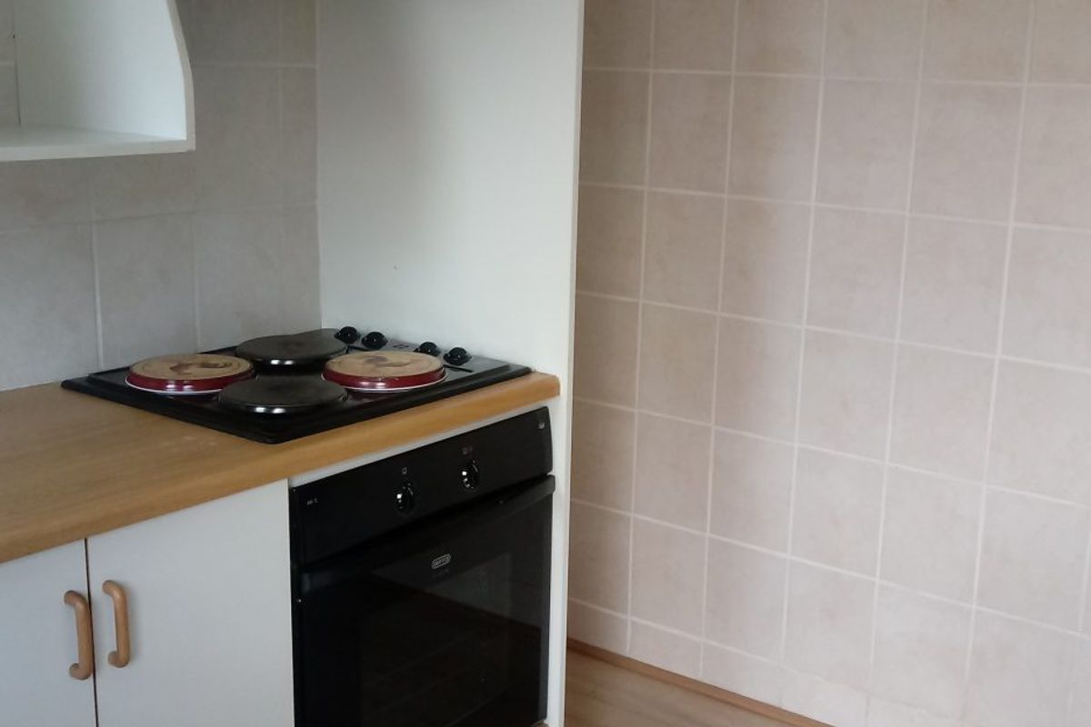 A functional kitchen area featuring a built-in oven, electric hob, tiled splashback, and laminate countertop with base cabinetry.