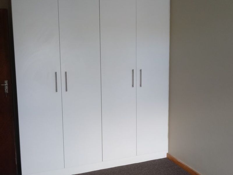 A clean bedroom interior featuring modern white built-in cupboards, a dark carpet, and a classic timber door.