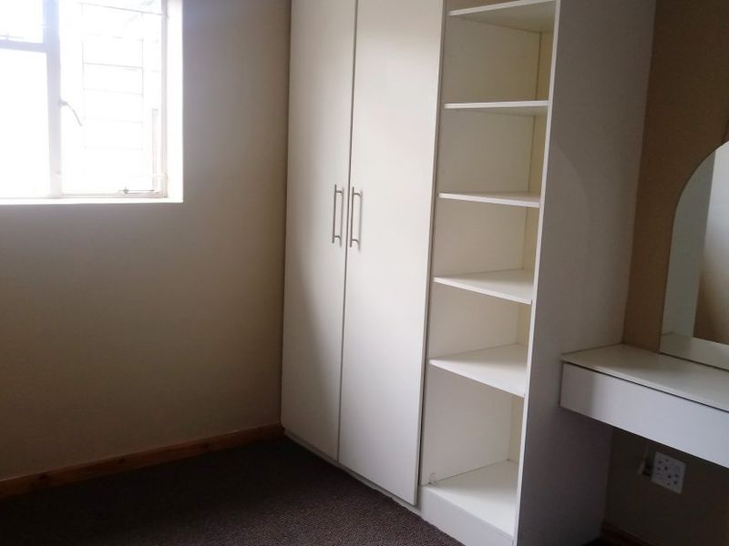 A clean bedroom featuring built-in white wardrobes, open shelving, and a wall-mounted vanity unit with a mirror.