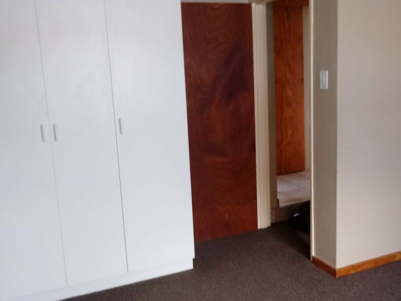 An empty bedroom featuring built-in white cupboards, carpeted flooring, and a wooden door leading to an adjacent space.