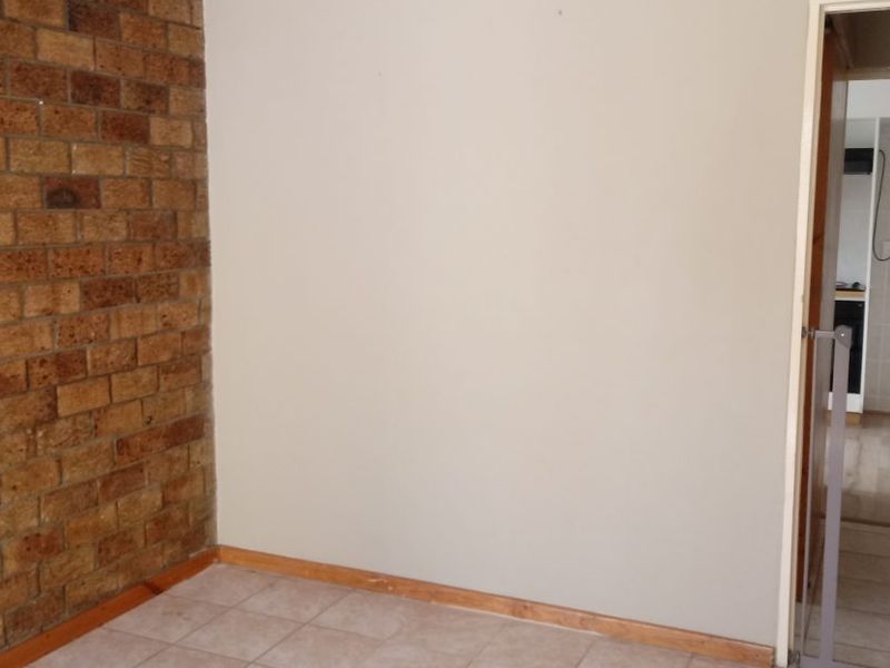 A neutral hallway space featuring an exposed brick accent wall, tiled flooring, and timber skirting boards, leading into an adjacent tiled area.