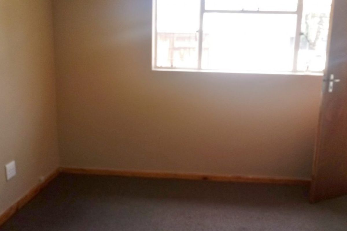 An empty bedroom featuring neutral wall paint, carpeted flooring, timber skirting boards, and a standard internal door.