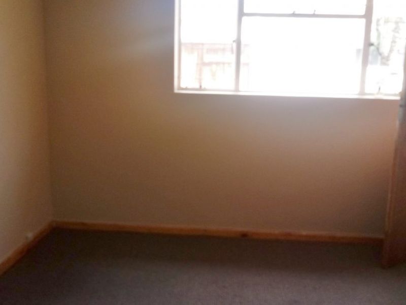 An empty bedroom featuring neutral wall paint, carpeted flooring, timber skirting boards, and a standard internal door.