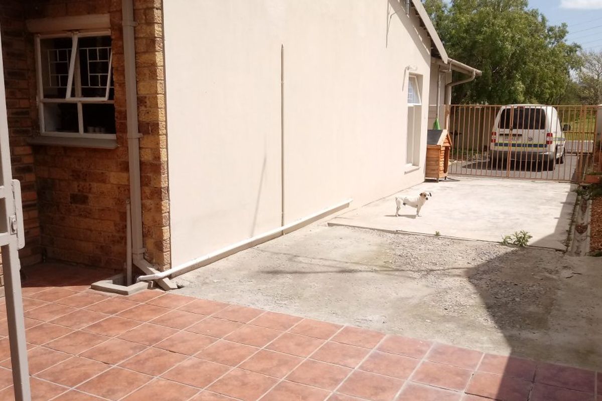 Rear exterior area featuring a tiled patio section and a concrete driveway leading to a gated entrance.