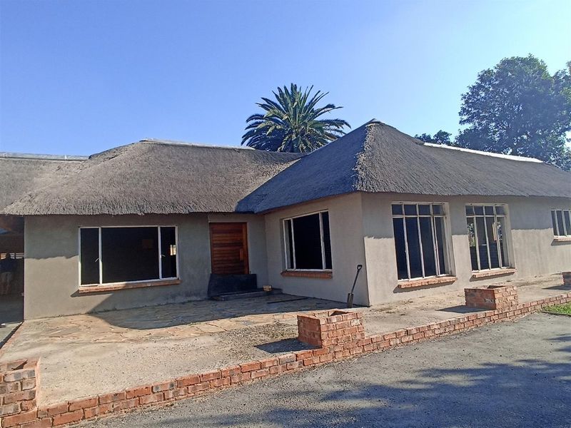 Front exterior view of a farm-style residence featuring a traditional thatched roof, plastered walls, and a paved entrance area.