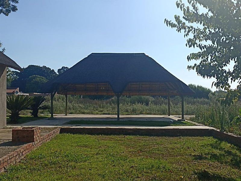 A spacious outdoor thatched-roof entertainment area set within a large garden, featuring a concrete base and open-sided structure.