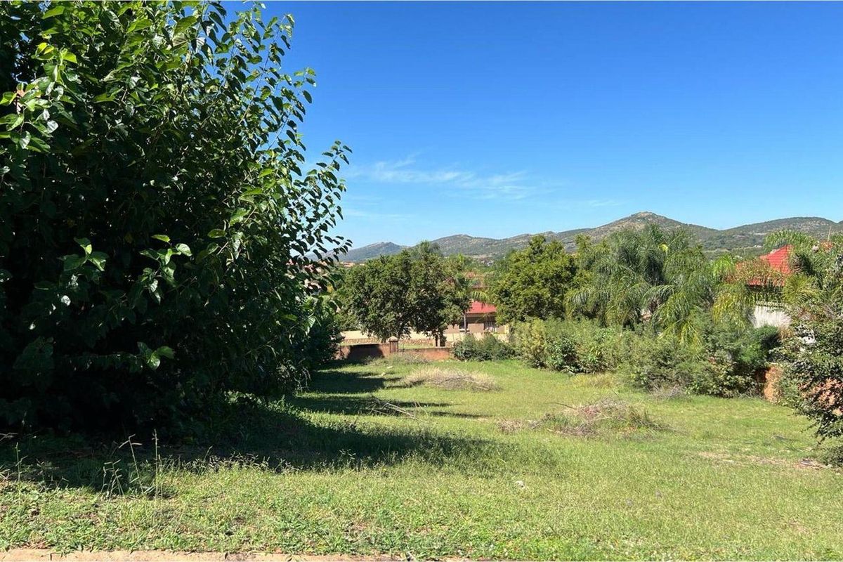 A scenic view of the vacant residential land featuring established trees, a grass lawn, and surrounding mountain vistas.