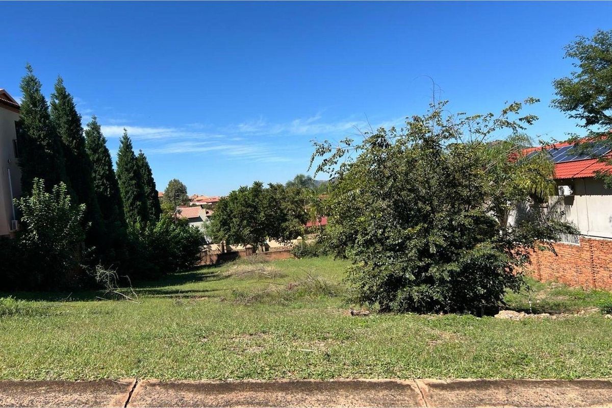 A vacant residential plot featuring established trees and boundary walls, offering a clear space ready for development in a suburban setting.
