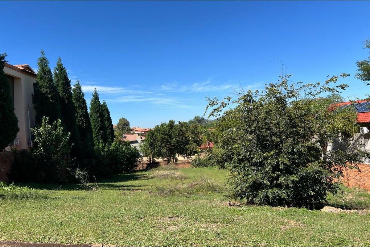 A vacant residential plot featuring established trees, a grassed area, and surrounding boundary walls in a residential neighborhood.