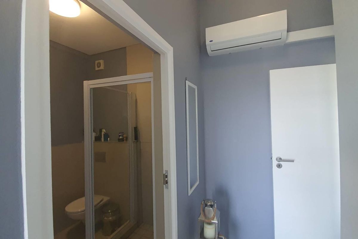 A view of a bathroom entrance featuring a wall-mounted air conditioning unit and a modern door frame.