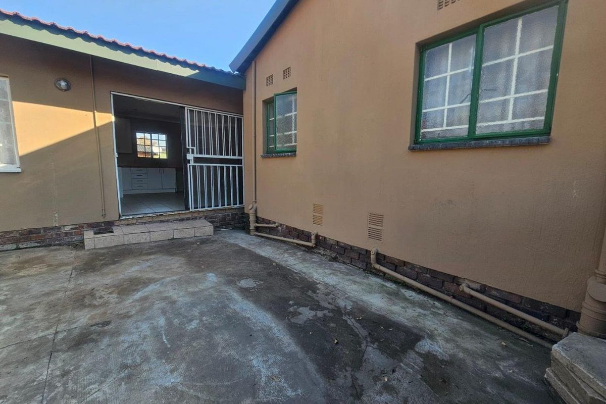 Rear exterior view of the house featuring a concrete patio area, security gate access, and visible external plumbing infrastructure.