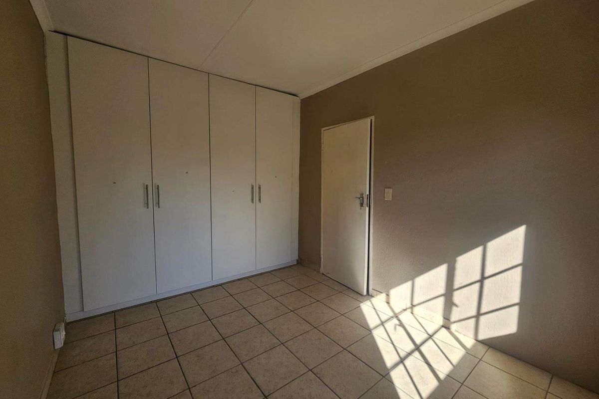An empty bedroom featuring tiled flooring, built-in cupboards, and neutral wall tones, offering a blank canvas for personalization.