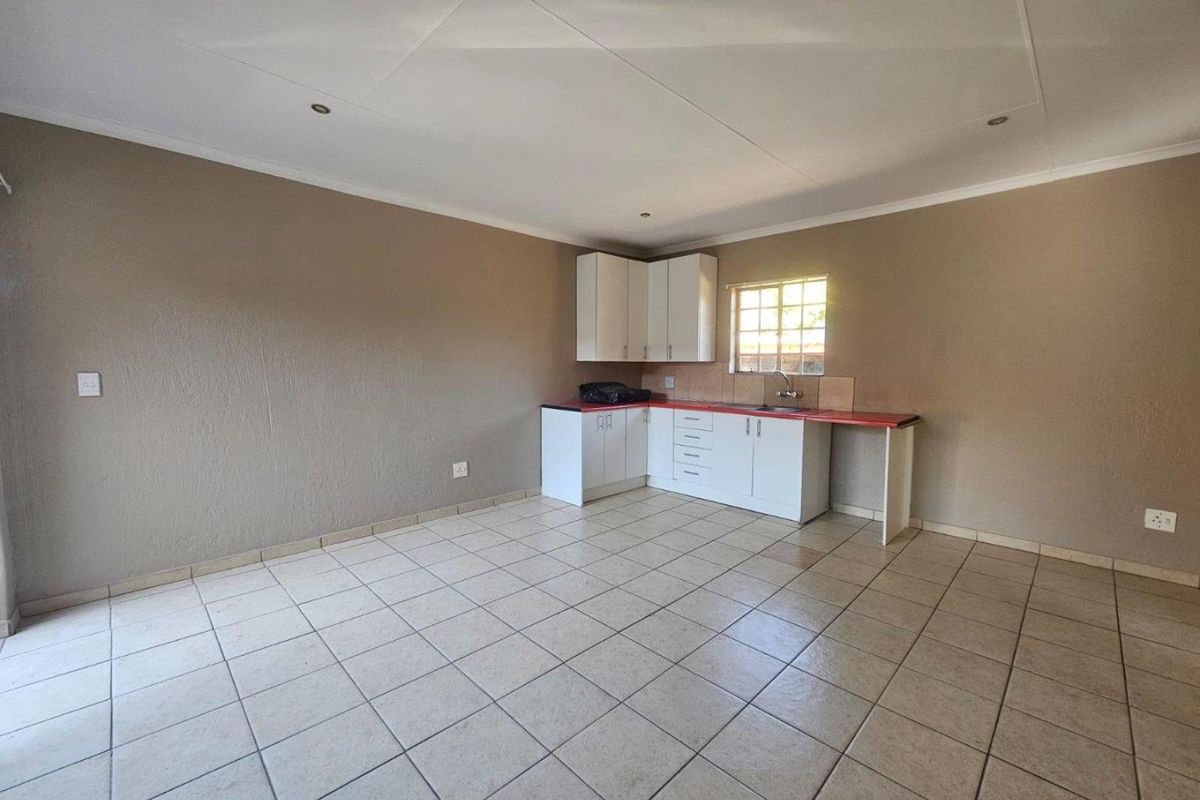 An empty kitchen area featuring tiled flooring, white built-in cabinetry, a red laminate countertop, and a stainless steel sink.