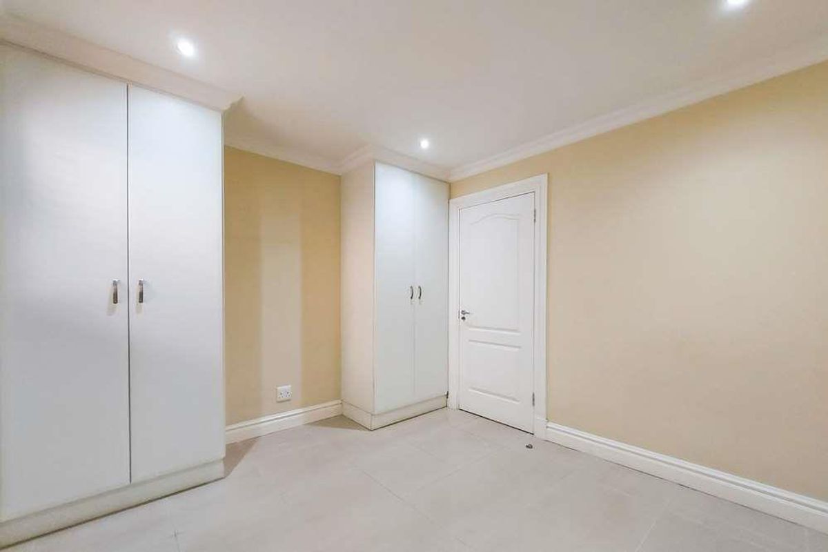 A bright bedroom featuring built-in white cabinetry, tiled flooring, recessed ceiling lighting, and a classic panelled door.