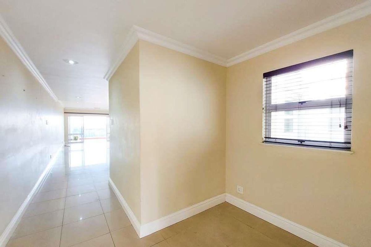 A bright, empty living area featuring neutral tiled flooring, crown molding, and large windows that allow for ample natural light.