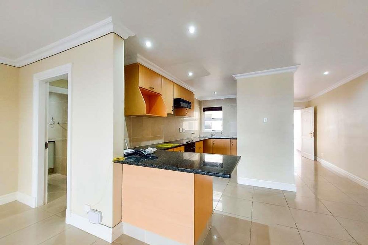 A functional kitchen featuring light wood cabinetry, dark granite countertops, and recessed ceiling lighting, seamlessly integrated into an open-plan living area.
