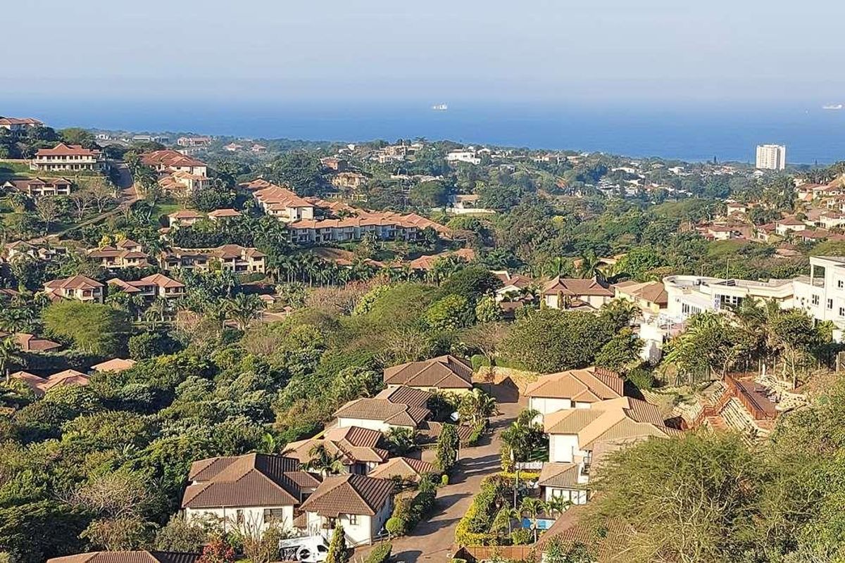 An elevated aerial view overlooking a residential estate with lush greenery and a distant ocean horizon.