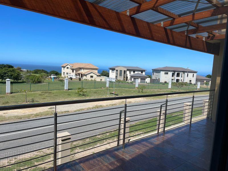 Covered balcony featuring a timber pergola, stainless steel balustrade, and tiled flooring, offering an elevated view of the surrounding estate and coastline.