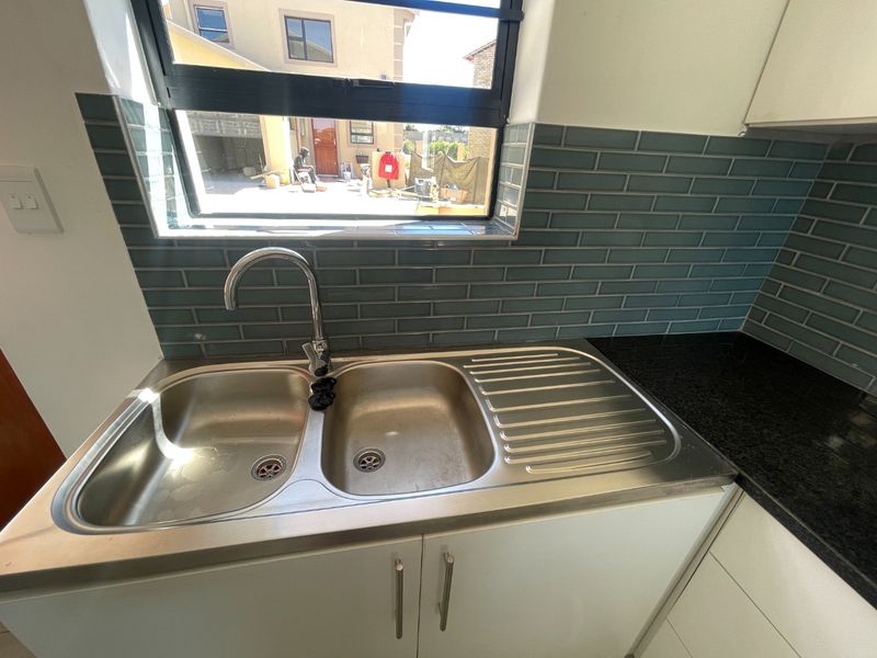 A clean kitchen area featuring a double bowl stainless steel sink, modern gooseneck mixer tap, granite countertops, and a stylish blue subway tile backsplash.