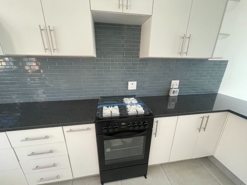 Modern kitchen featuring white cabinetry, black granite countertops, a stylish grey subway tile backsplash, and a clean freestanding oven.