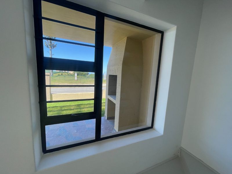 View from an interior room looking out onto a covered patio area featuring a built-in braai and tiled flooring.