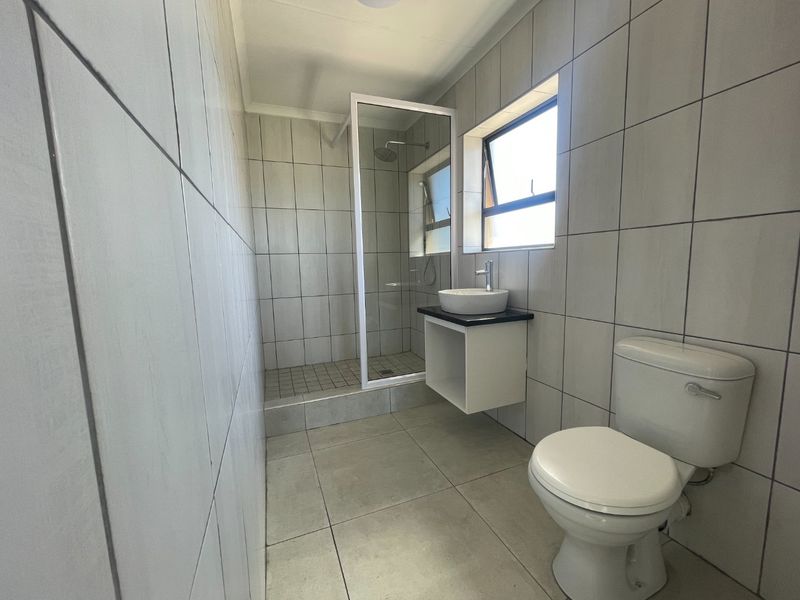 A clean and functional bathroom featuring a walk-in shower, a modern vessel sink with a vanity cabinet, and neutral floor-to-ceiling wall tiles.